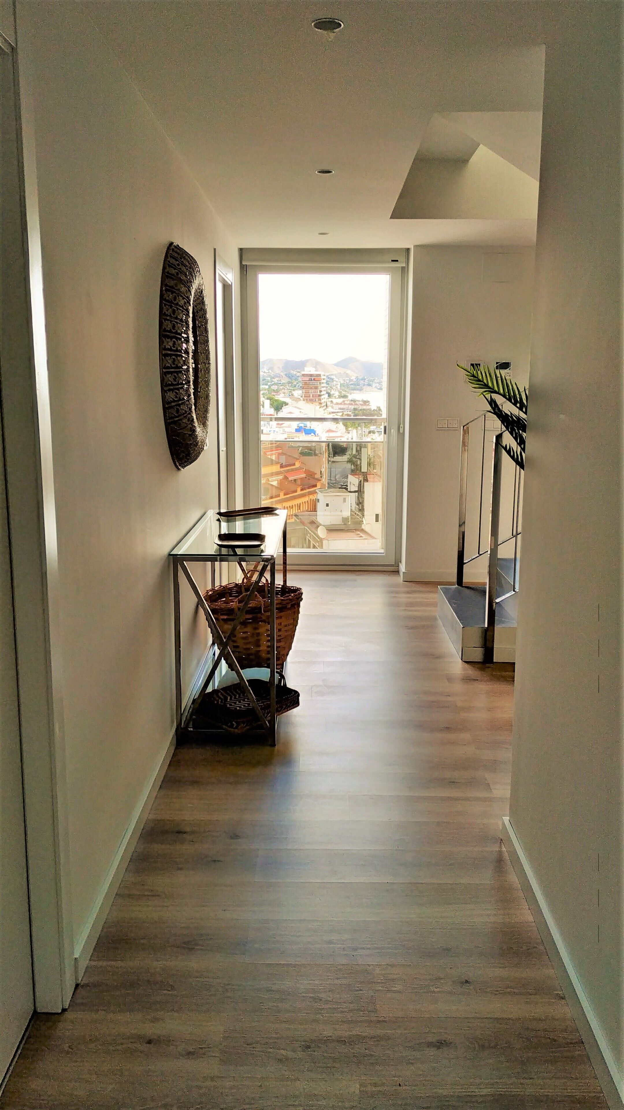 Un pasillo con vista al exterior, una cesta y una planta.