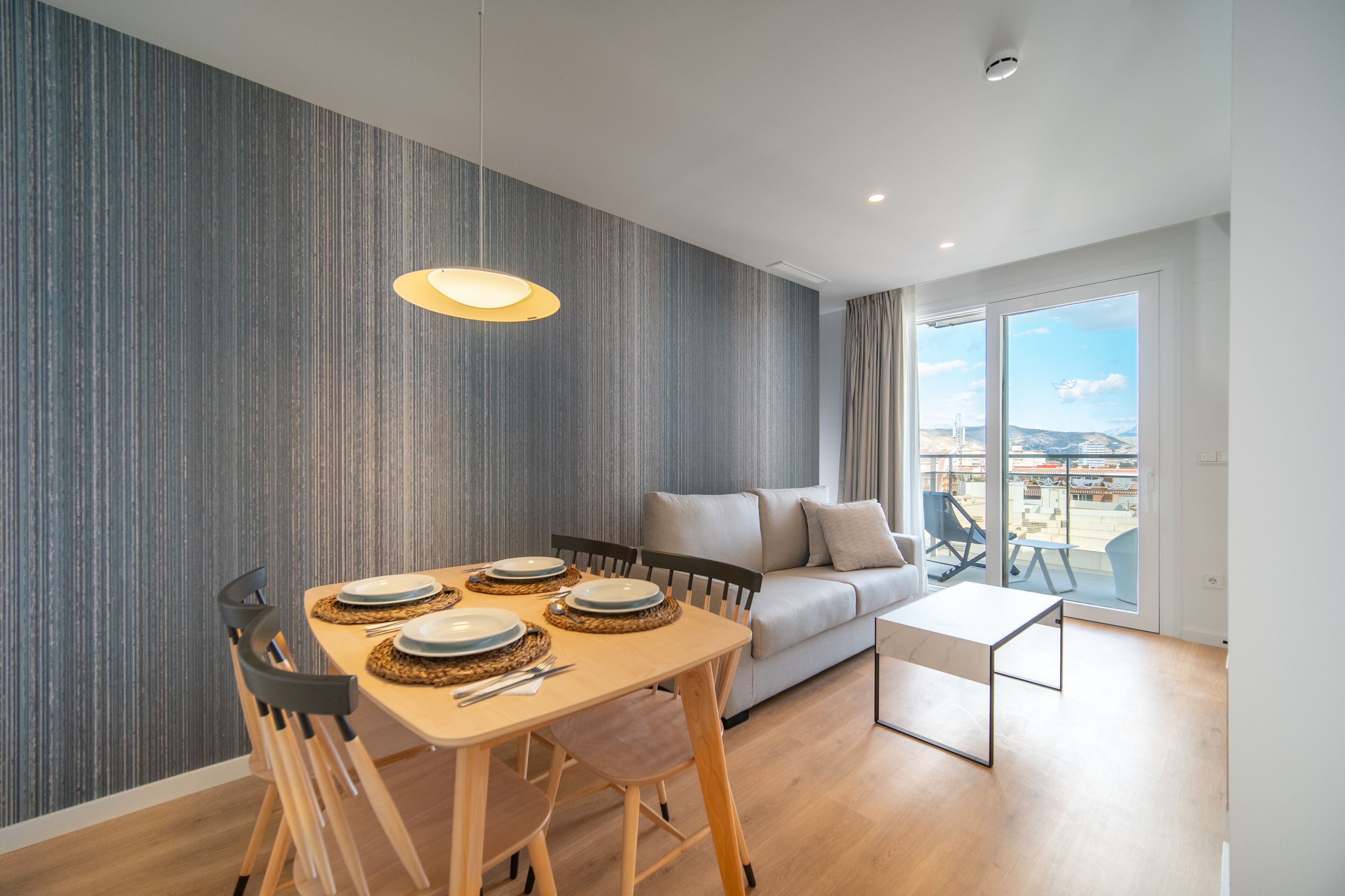 A modern living room with a dining area, a sofa, and a balcony with a view.