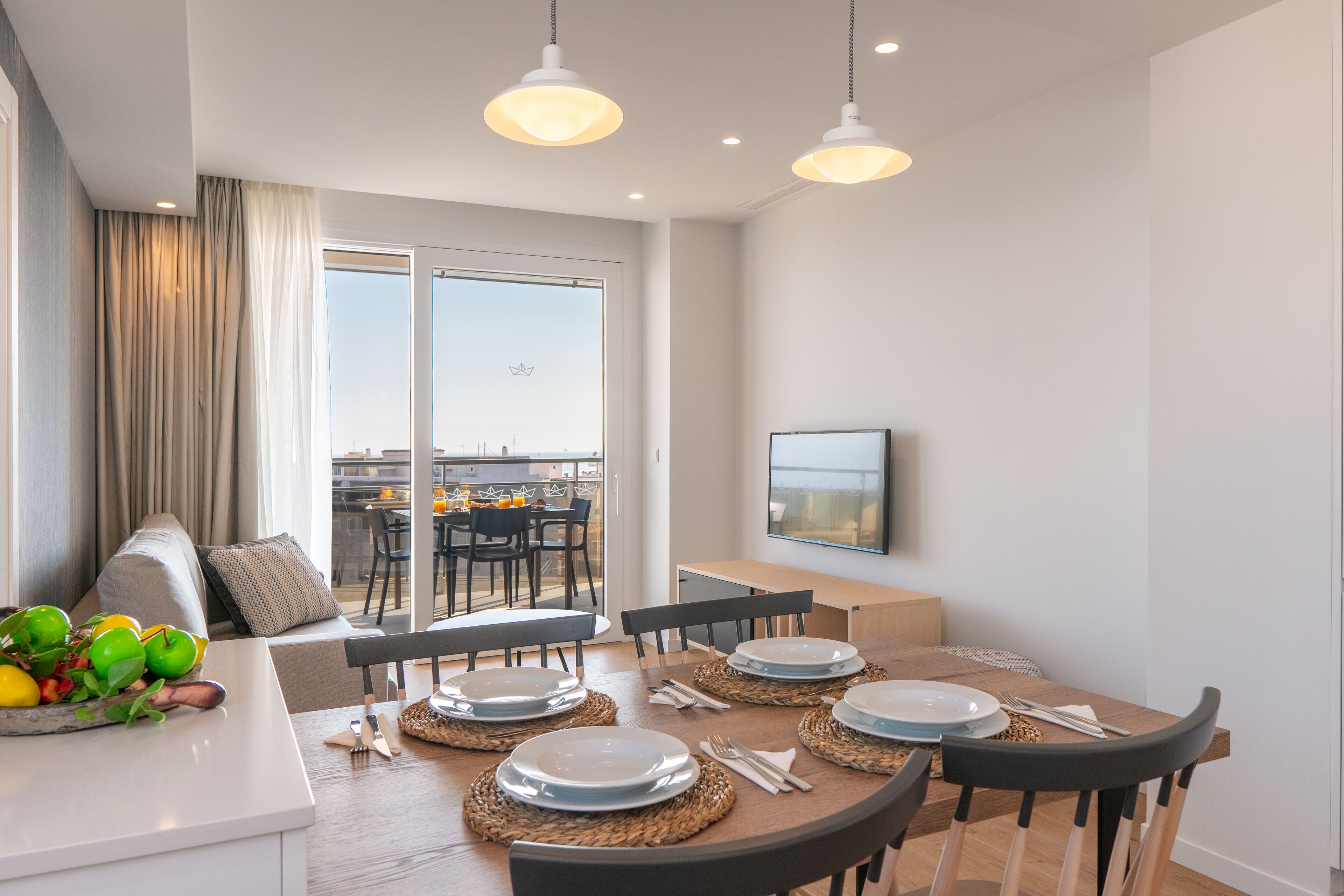 Un espace repas moderne avec une table ronde pour quatre personnes, un canapé avec des coussins et une grande fenêtre offrant une vue sur la ville.