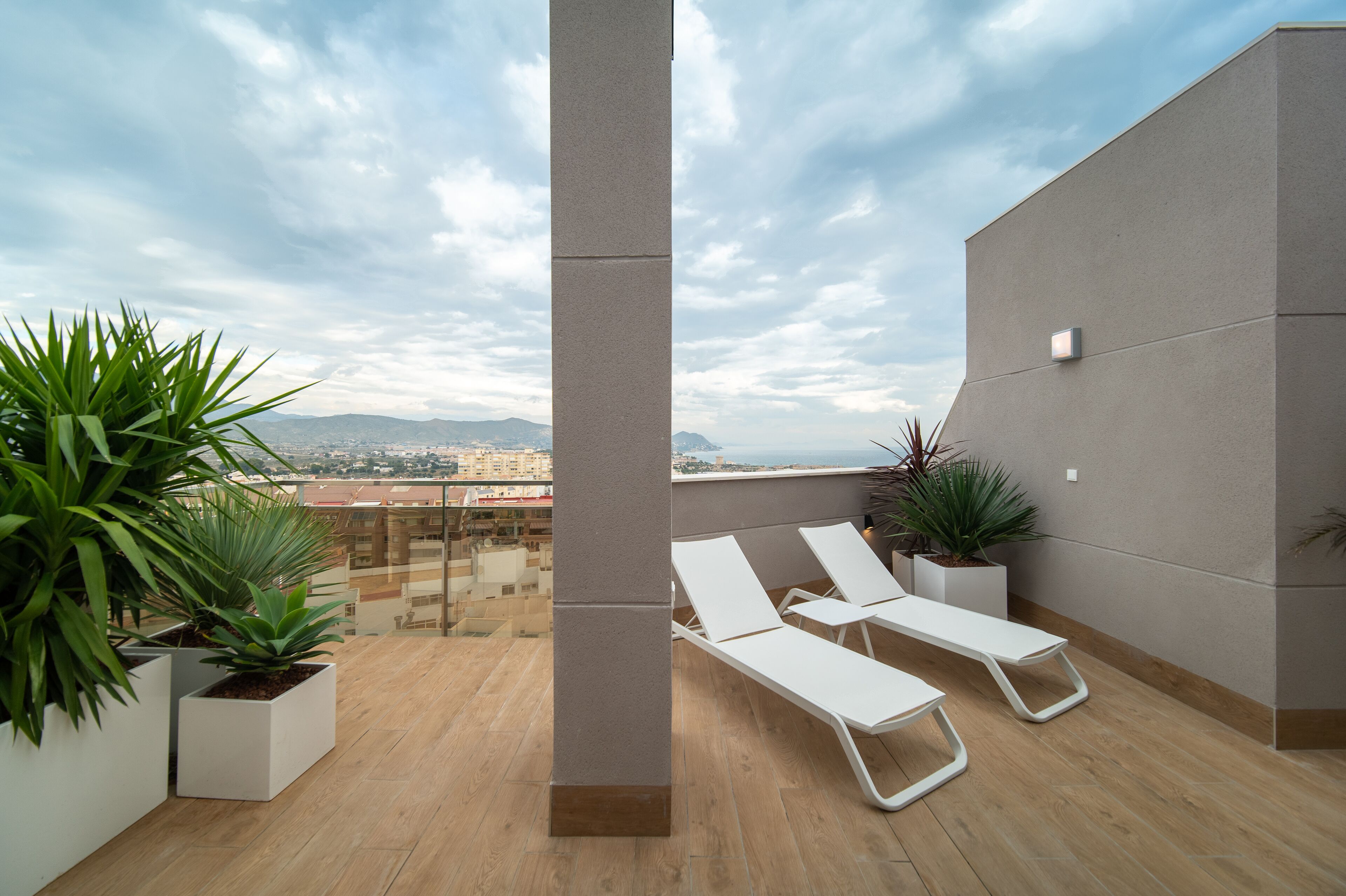 A rooftop terrace with white lounge chairs, potted plants, and a view of the cityscape.