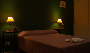 A single bed with a brown bedspread in a dimly lit room with green walls. There are two bedside tables, each with a lamp and a small potted plant. - Hostel Casa Borges (Adrogué)