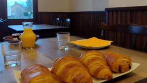 Une table de petit-déjeuner avec des croissants, un verre de jus d’orange et un verre d’eau.