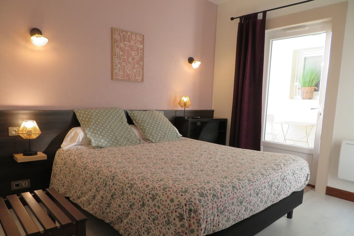 Une chambre à coucher comprenant un lit, deux lampes de chevet, une table de chevet, un banc en bois, une couvre-lit à motifs et une œuvre d’art murale.