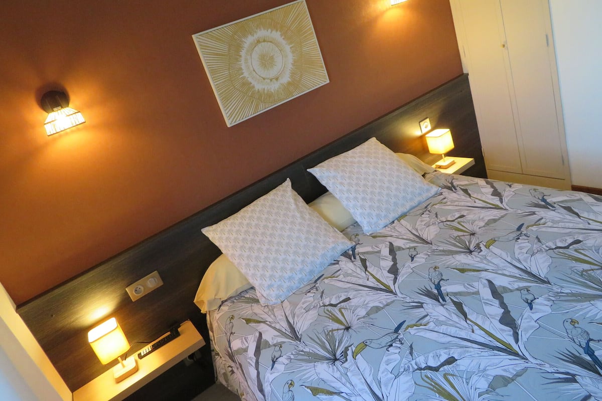 Une chambre d’hôtel comprenant un lit, deux lampes de chevet, un luminaire fixé au mur et une table de chevet avec une lampe.