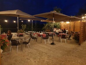 Un espace extérieur aménagé en terrasse, avec des tables et des chaises placées sous de grands parasols, entouré de murs en bois et de plantes en pot.