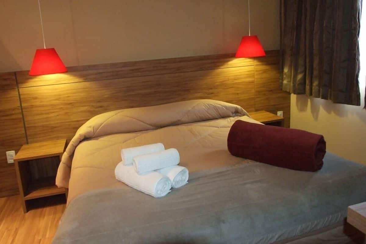A neatly made bed with a wooden headboard, two bedside tables, and red lamps.