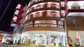 Um hotel com vários andares, varandas, entrada de vidro e fachada bem iluminada.