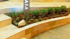 Uma área de recepção de hotel com um pilar de mármore, plantas internas e uma área de estar vermelha.