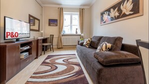 A living room with a sofa, a TV, a painting, and a window with curtains. - P&O Apartments Freta 2 (Warsaw)