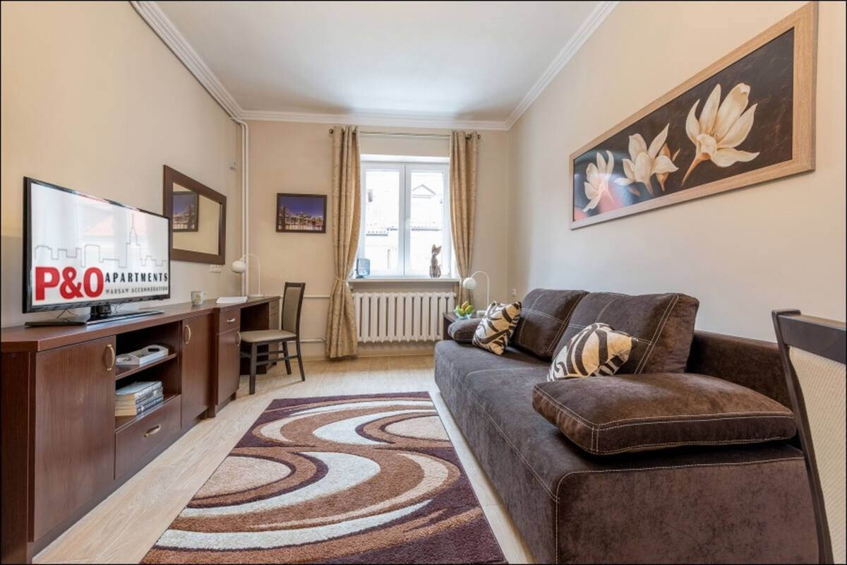 A living room with a sofa, a TV, a painting, and a window with curtains.