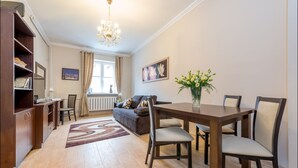 A dining area with a wooden table and chairs, a chandelier, a sofa, and a radiator. - P&O Apartments Freta 2 (Warsaw)