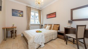 A bedroom with a bed, a desk, a chair, a window with curtains, and a chandelier. - P&O Apartments Freta 2 (Warsaw)