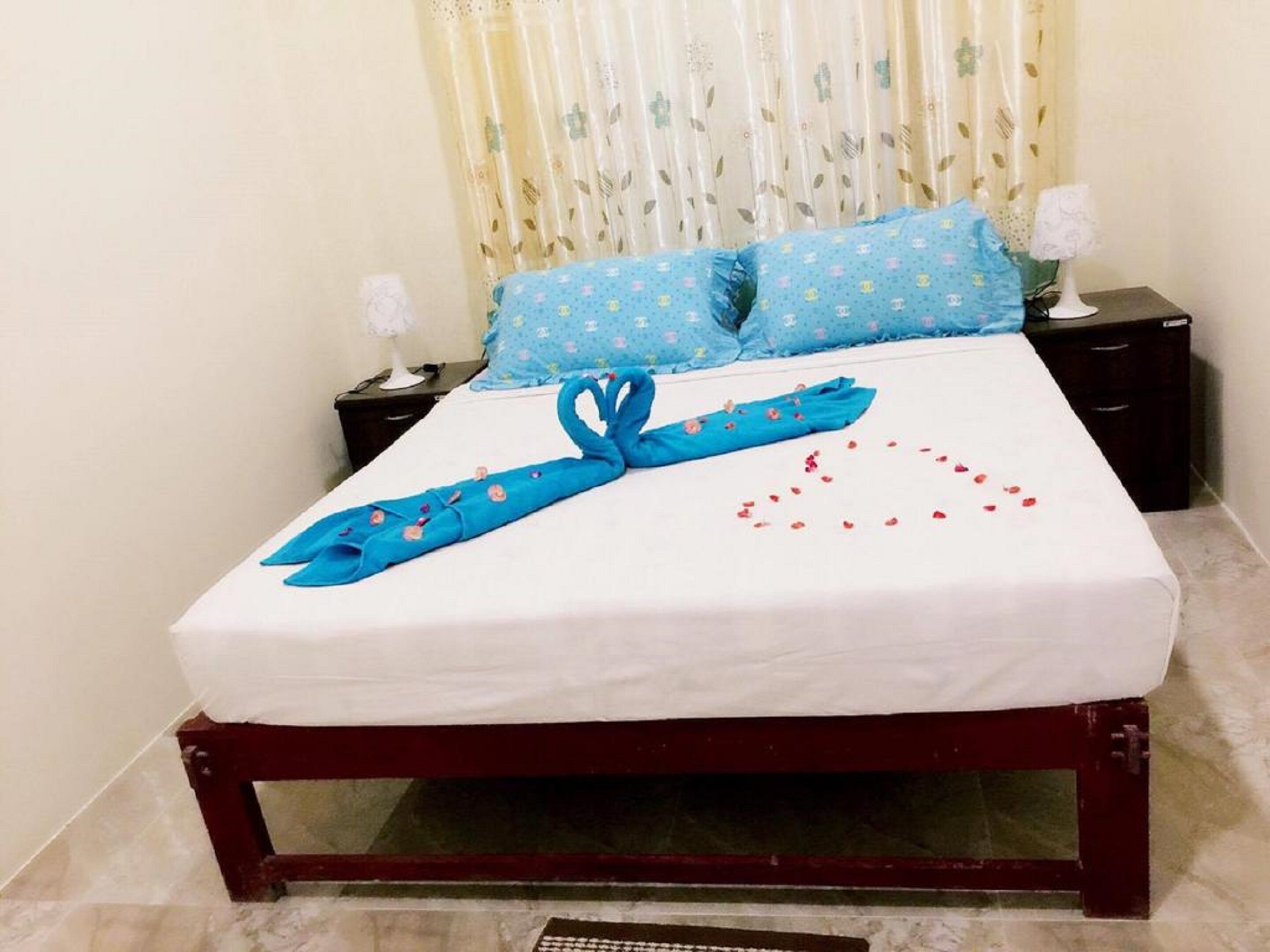 A neatly made bed with a blue towel and a heart-shaped arrangement of rose petals on the bedspread.