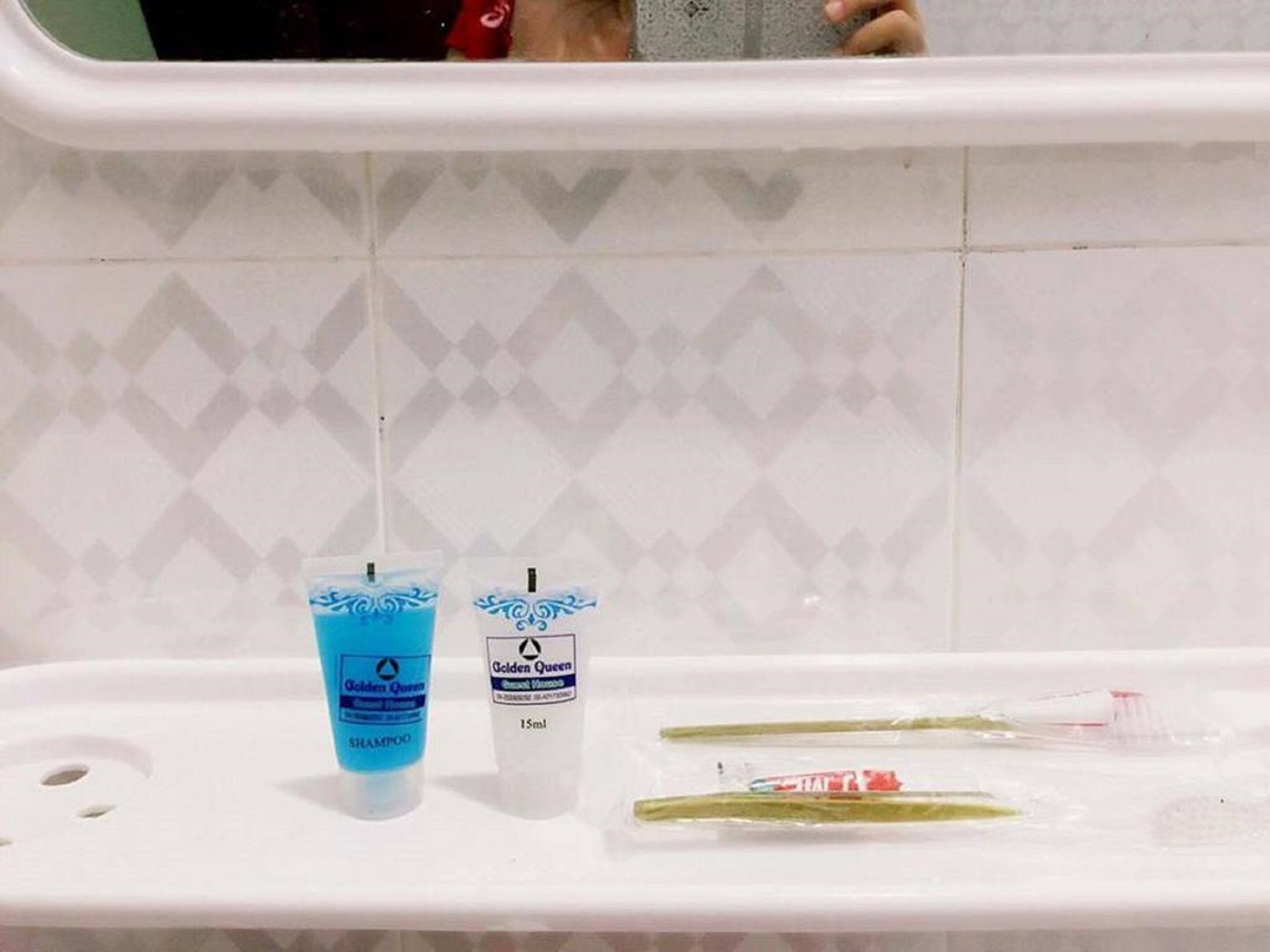 A bathroom with a white sink, two bottles of shampoo, and a toothbrush in a plastic bag.