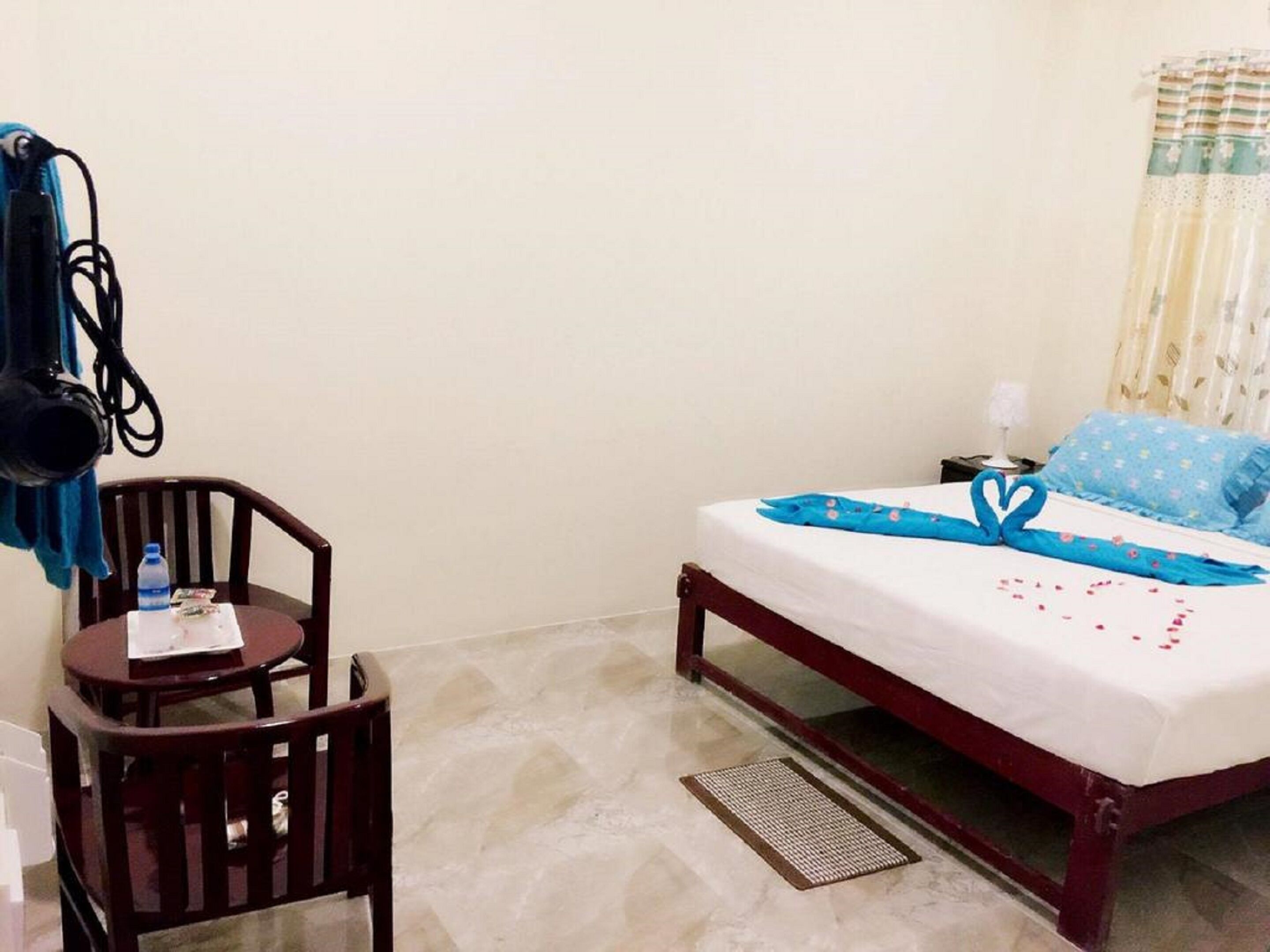 A hotel room with a bed, a small table with a chair, a water bottle, and a power outlet.