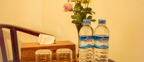 A wooden tray with three glasses, two water bottles, and a vase with flowers on a table.