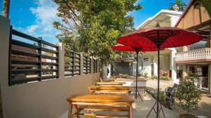 Outdoor wooden tables and benches, a red umbrella, and a building with a sign. - Golden Queen Guest House (Ngapali)