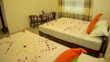 Two single beds with white bedspreads and rose petal arrangements, a wooden headboard, and a small table with a vase of flowers.