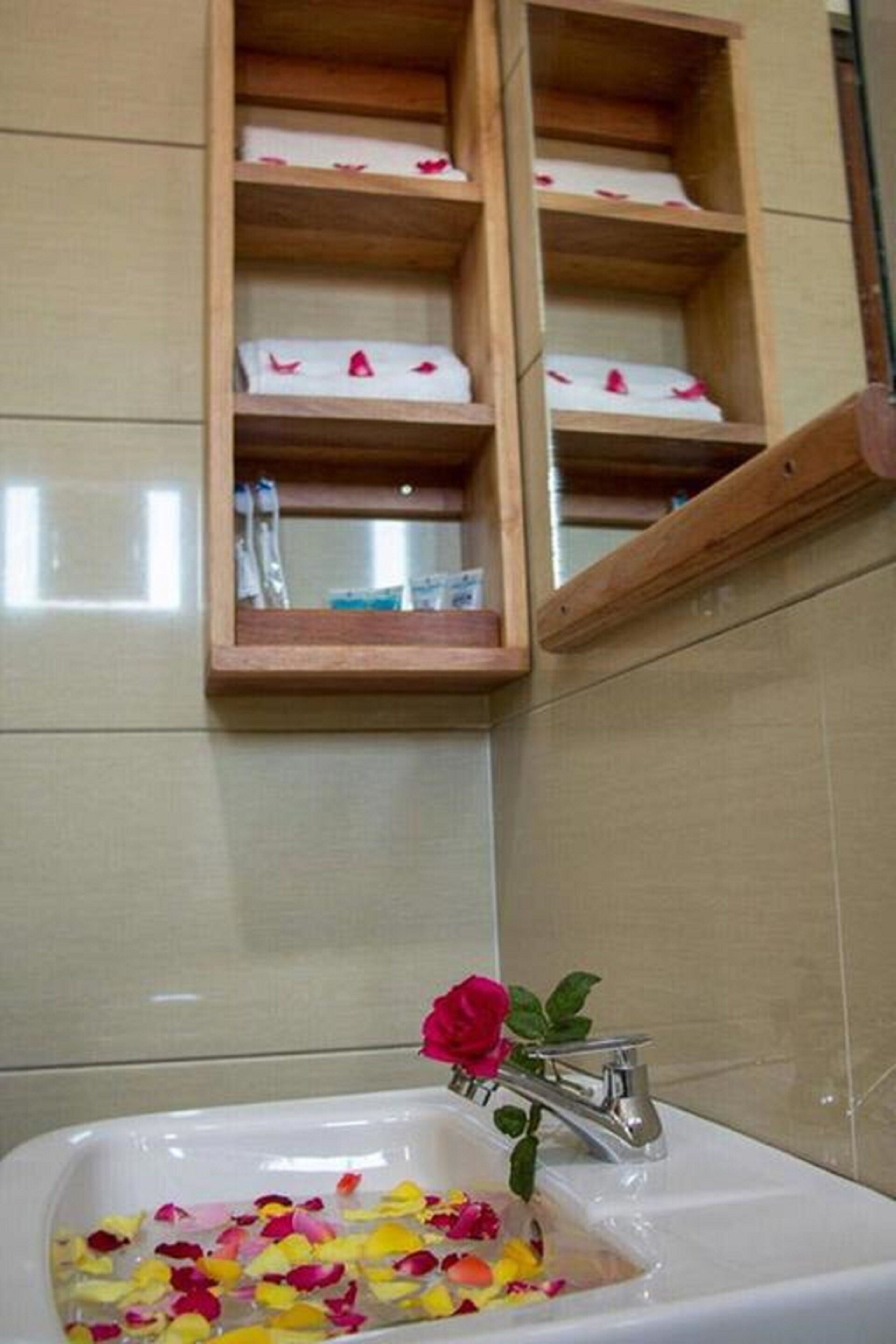Een badkamer met een wit wastafelmeubel, houten planken erboven en een enkele rode roos in de wastafel.