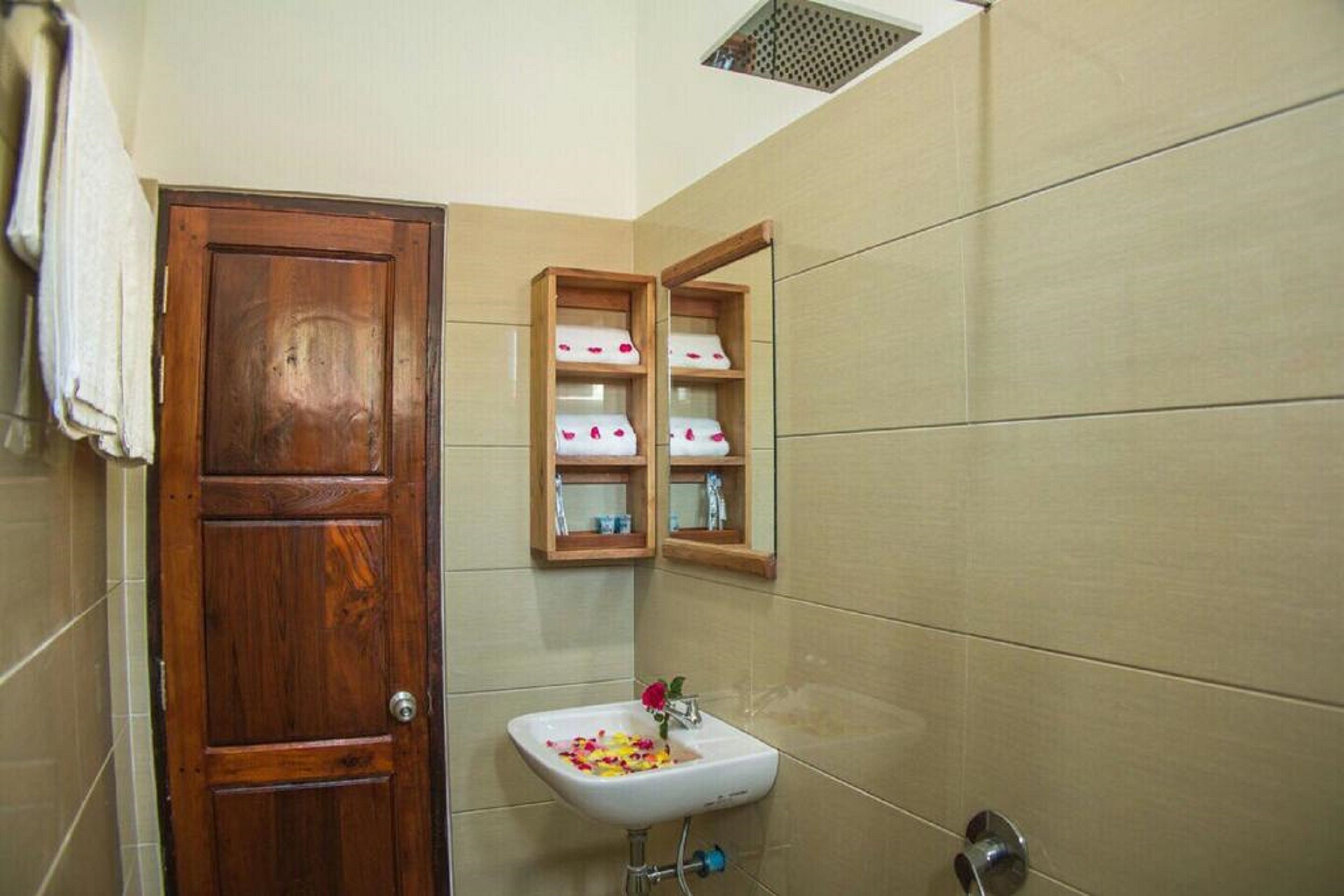A bathroom with a wooden door, a white sink with a flower, and wooden shelves above it.