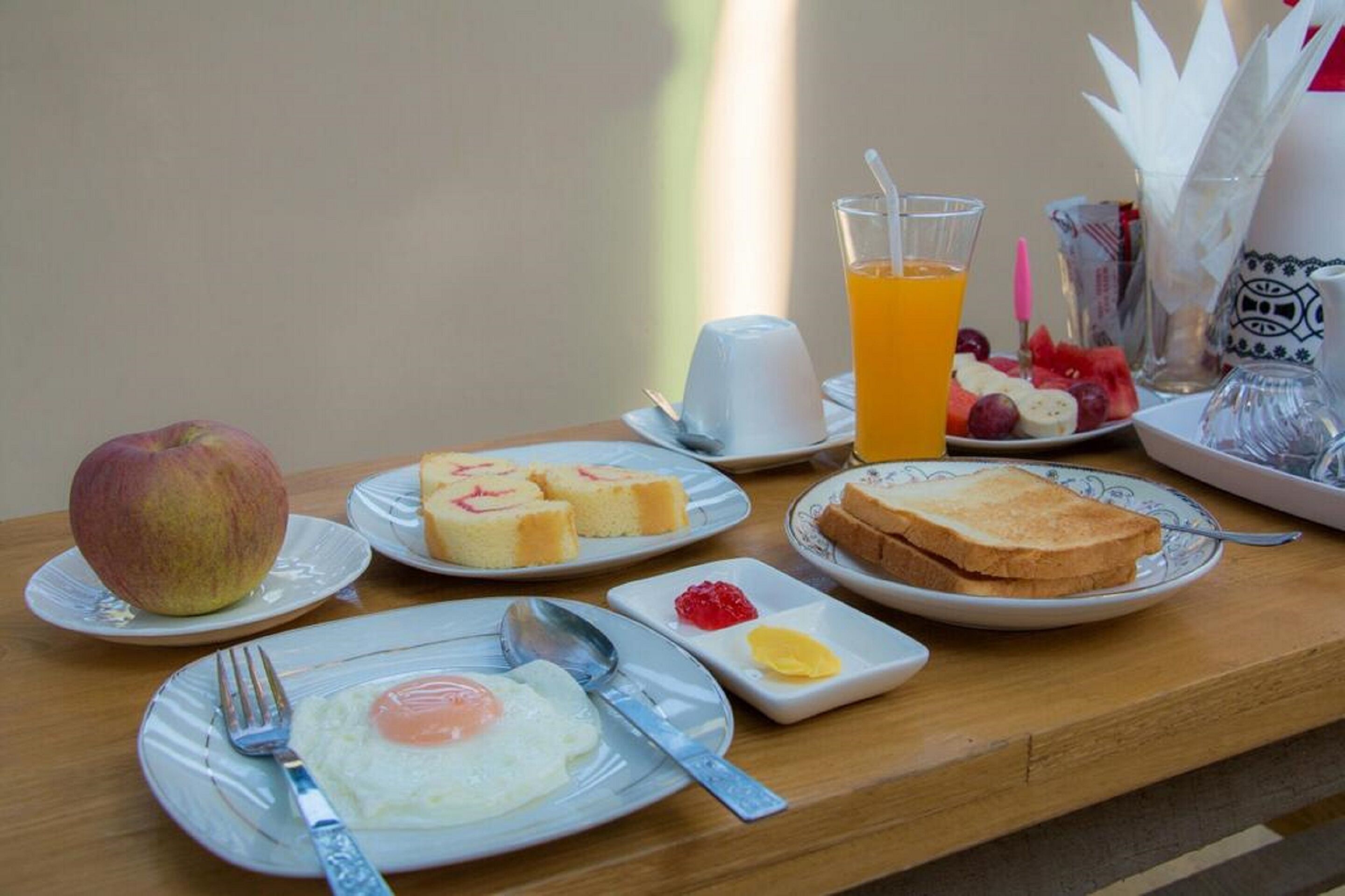 Ein Frühstückstisch mit Toast, Eiern und Obst, ein Glas Orangensaft und eine Wasserkaraffe.