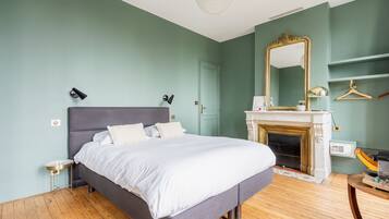 A bedroom with a bed, a mirror, a fireplace, and a wooden floor.