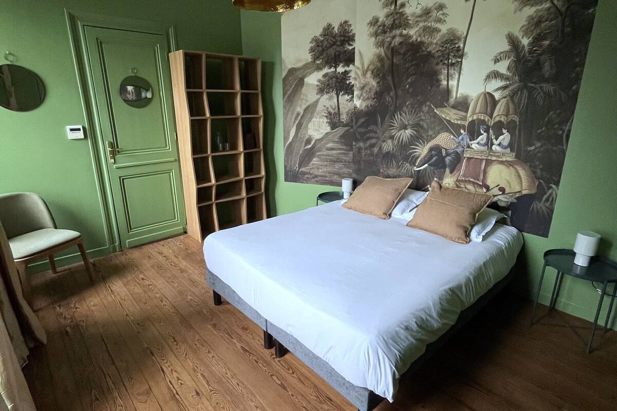 Un dormitorio con una cama grande, una pared verde, un mural y suelo de madera.