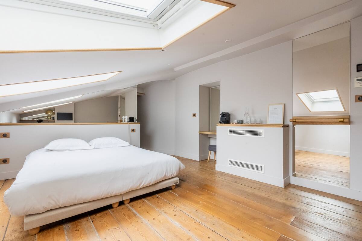 Un dormitorio moderno con tragaluz, suelo de madera, cama, escritorio y espejo.