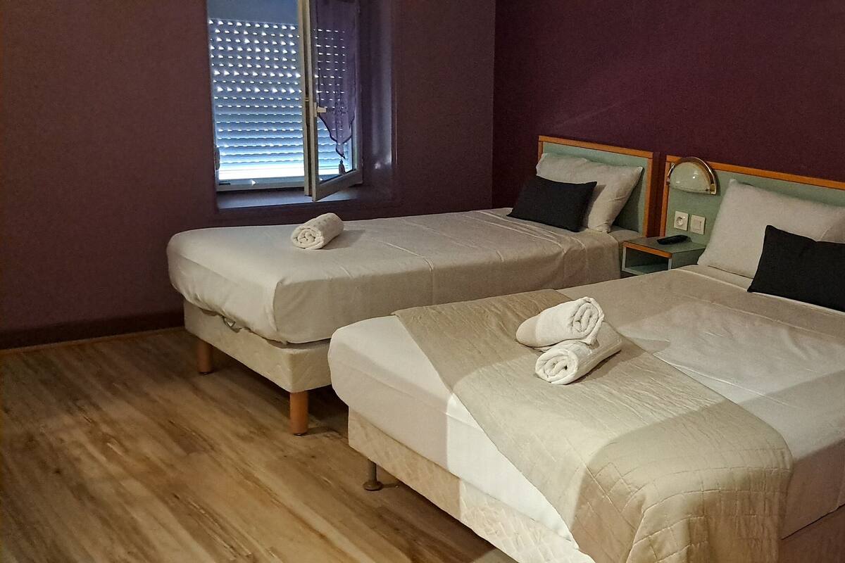 Two single beds with white linens and towels, a wooden floor, and a window with blinds.