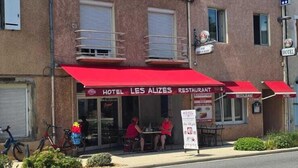 Un hotel con tenda rossa e insegna che recita 'HOTEL LES ALIZES RESTAURANT'.