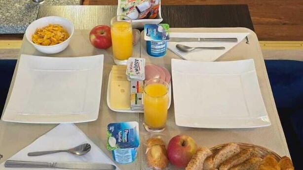 Colazione servita con cereali, frutta, succo e pasticcini su un tavolo in camera d'albergo.