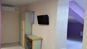 Una stanza con un letto, un comodino, una TV a muro e una porta che dà su un'altra stanza.
