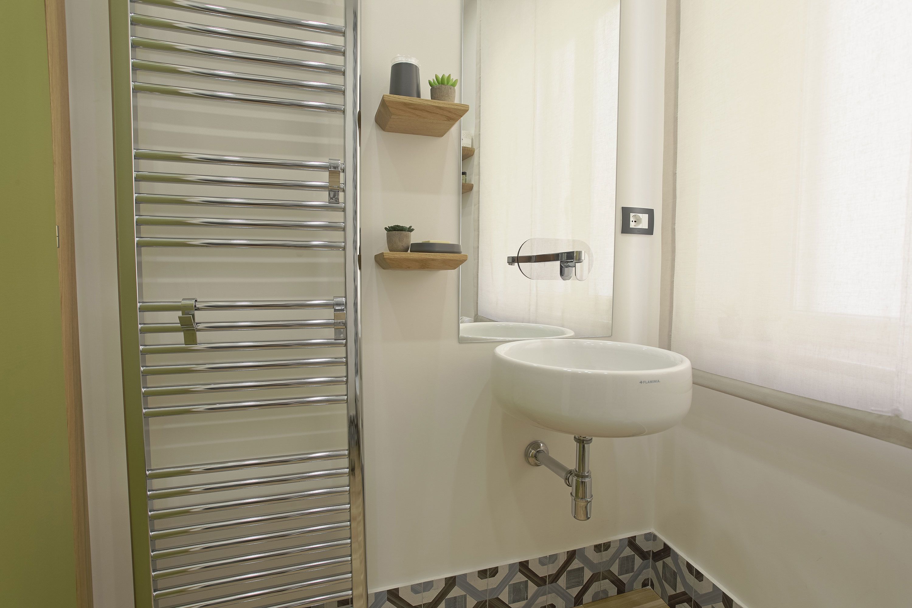 A bathroom with a white sink, a mirror, and a towel rack. There are wooden shelves with small plants.