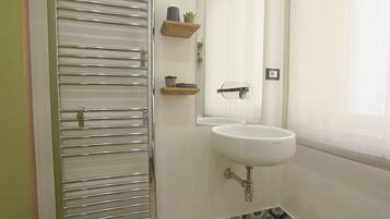 A bathroom with a white sink, a mirror, and a towel rack. There are wooden shelves with small plants.