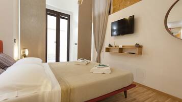 A hotel room with a bed, a TV mounted on the wall, a wooden shelf with a plant, and a large mirror.
