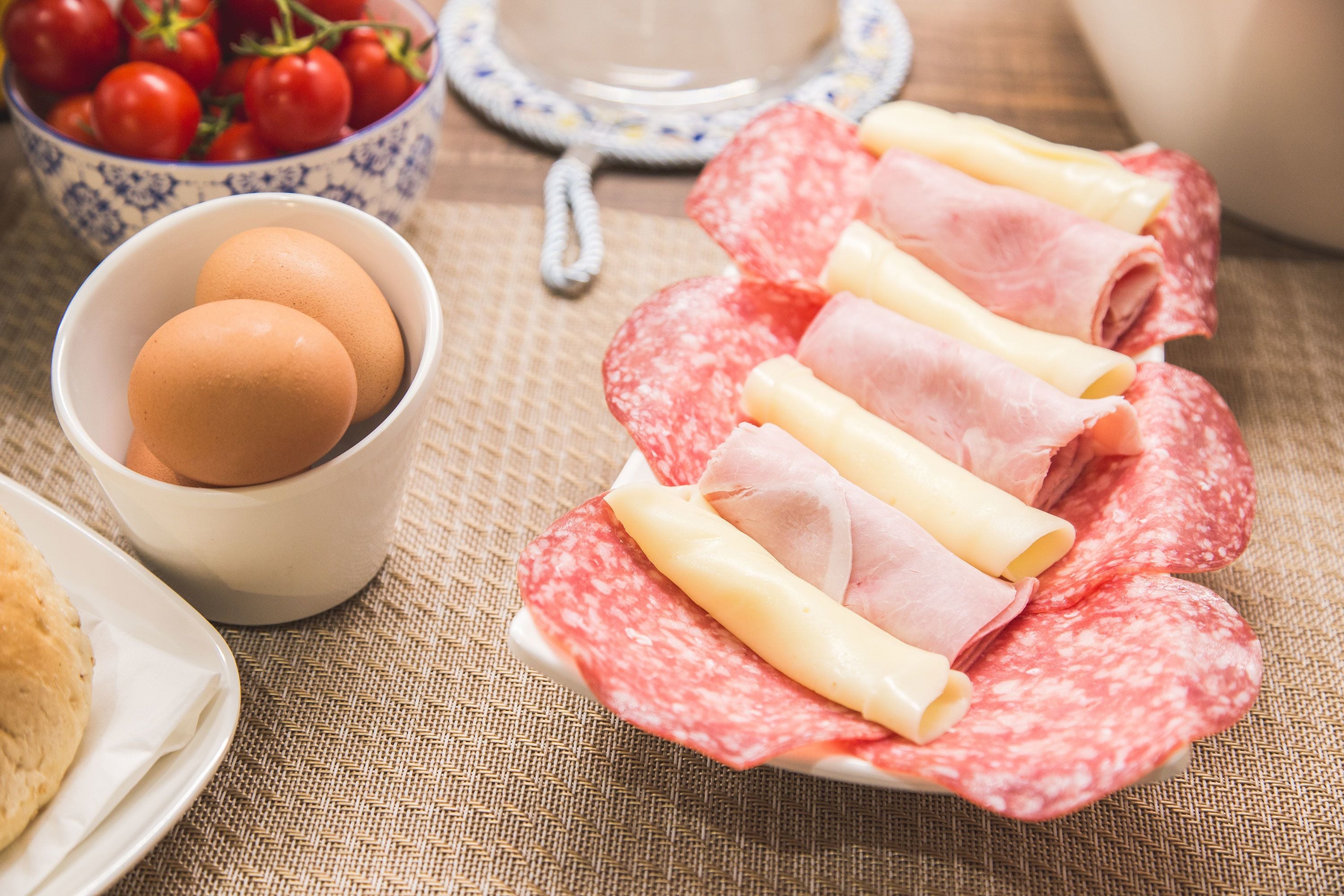 A plate of sliced salami and cheese, a bowl of eggs, and a bowl of tomatoes on a table.