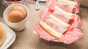 A plate of sliced salami and cheese, a bowl of eggs, and a bowl of tomatoes on a table.