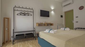 Habitación de hotel con cama, televisor, perchero, repisa con artículos de aseo y radiador.
