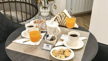A breakfast setup on a round table with a placemat, including croissants, orange juice, coffee, and cookies.