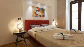 A modern hotel room with a red headboard, a large abstract painting, a round bedside lamp, neatly folded towels, and a wooden floor.