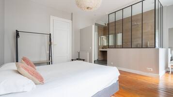Een slaapkamer met een bed, een houten vloer, een witte deur en een zichtbare badkamer door een open deur.