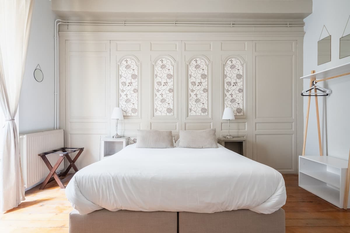 A bedroom with a large bed, a nightstand, a dresser, and a window with decorative glass panels.