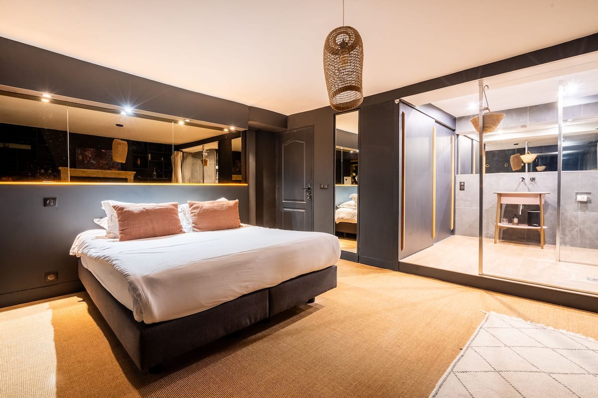 A modern bedroom with a large bed, a glass shower enclosure, and a visible bathroom.
