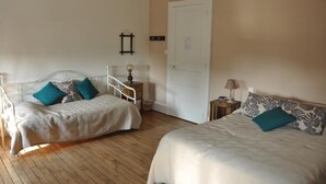 Una habitació amb dos llits, una porta blanca, una taula petita amb una làmpada i un mirall fixat a la paret.