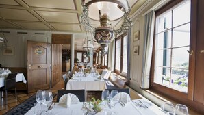 A dining area with tables set for service, large windows, and a decorative ceiling fixture. - Gasthof zur Sonne (Stafa)