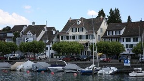 A marina with boats docked, a building with a sign 'Gasthof zur Sonne', and a parking sign. - Gasthof zur Sonne (Stafa)