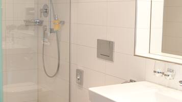 A modern bathroom with a glass-enclosed shower, a white toilet, and a sink with a mirror above it.
