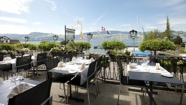 An outdoor dining area with tables set for a meal, overlooking a body of water and mountains. - Gasthof zur Sonne (Stafa)