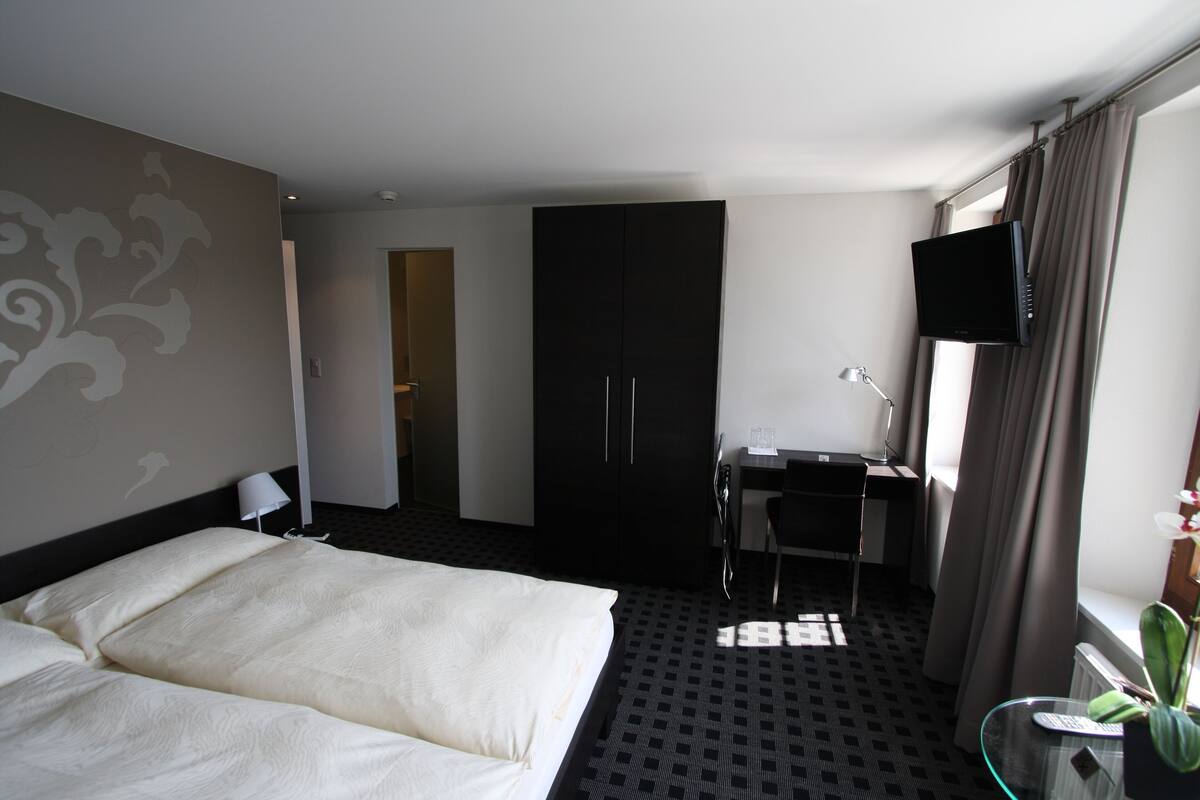 Ein Hotelzimmer mit Bett, Schreibtisch, Stuhl, Fernseher und einem Fenster mit Vorhängen.