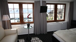 A hotel room with a bed, a sofa, a TV, a window with curtains, a radiator, and a small table with a plant. - Gasthof zur Sonne (Stafa)